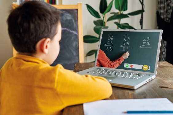 Child back to school, sitting at a desk using a laptop for an online math class