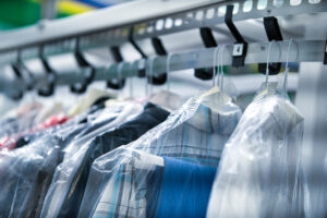 Clothes covered in plastic are hanging on hangers and moving along a conveyor system in a dry cleaning facility—reminding us of how some wonder, do mothballs work to keep bugs out of the house?