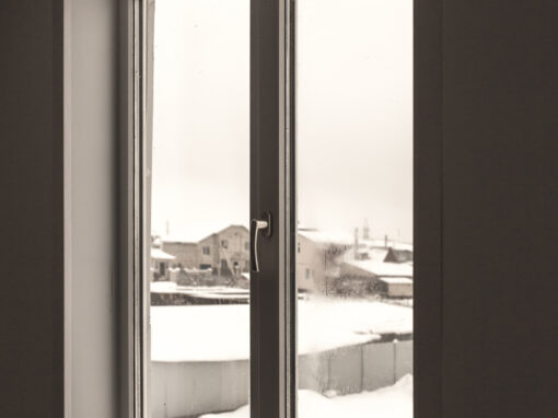 Double-paned window with a white frame overlooking a snowy residential area; houses and fences are visible outside.