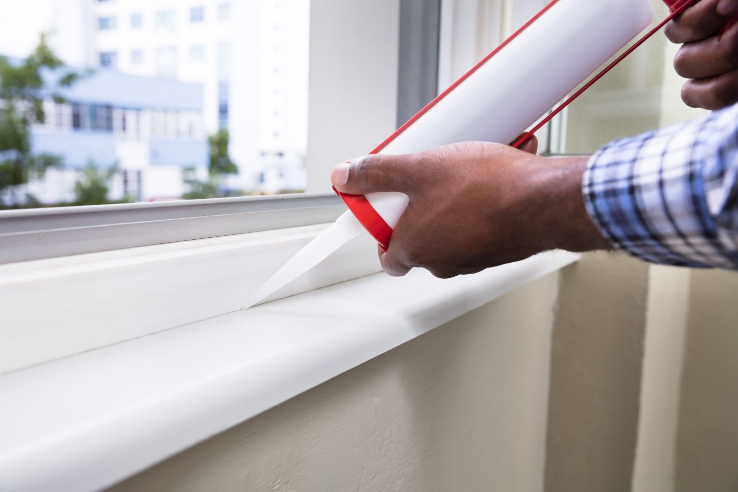 Hands applying caulk along a window frame to seal gaps and improve insulation