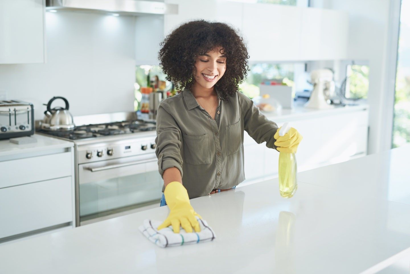 Person wearing gloves wipes a kitchen counter while holding a spray bottl
