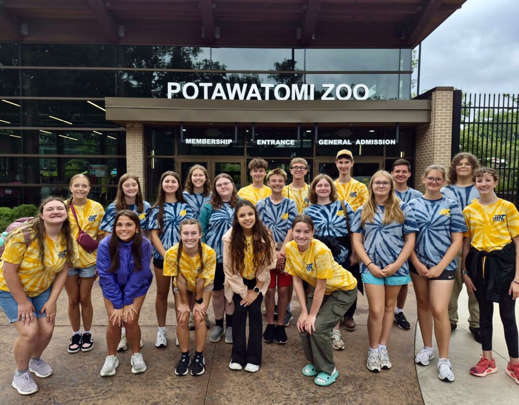 A group of young people in matching shirts poses and smiles in front of the Potawatomi Zoo entrance.